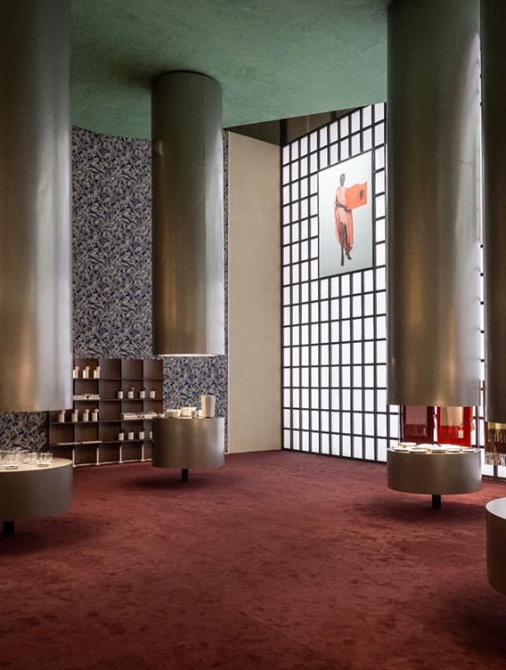 Tall cylindrical columns framing a product display room with red carpet, patterned walls and a large fashion portrait